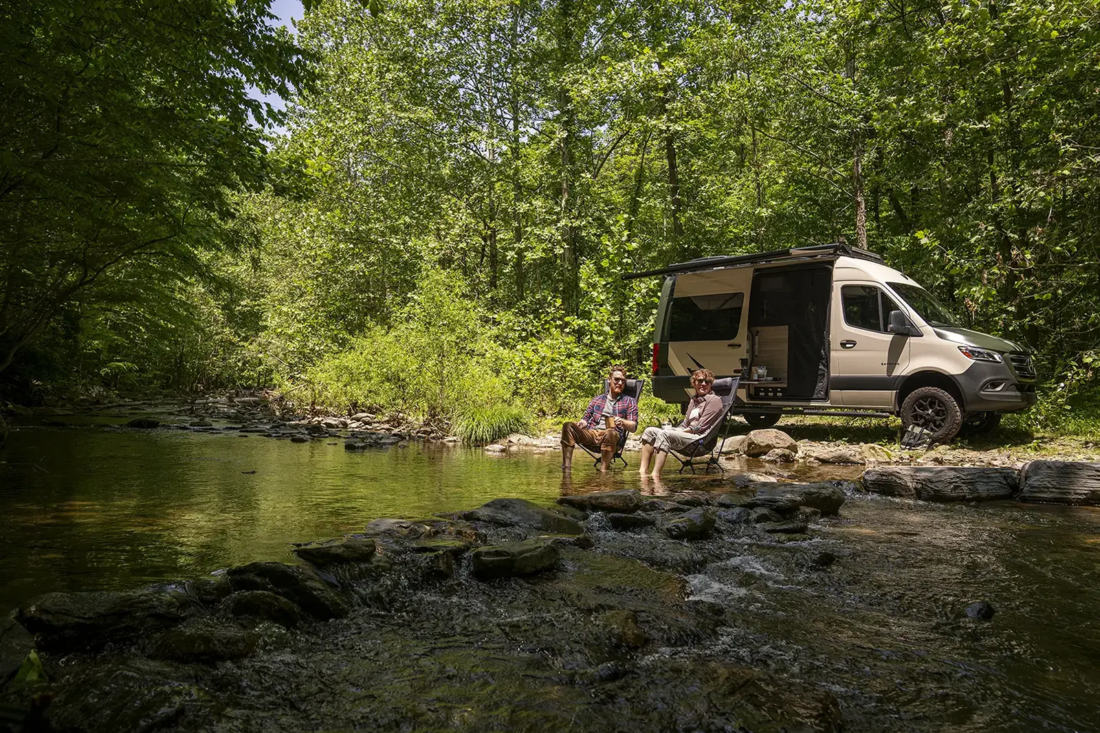 Couple relaxing by a stream beside their camper van